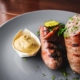 two sausages on a plate with mustard on the side